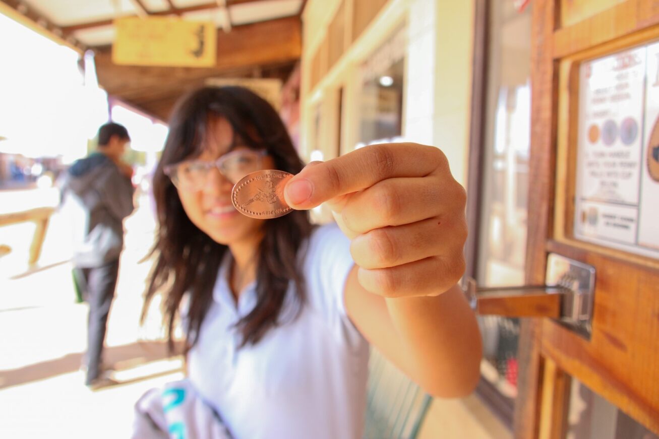 A student smiles and holds her engraved coin to the camera.